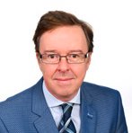 Portrait photo of man with navy suit jacket, light blue shirt, tie and glasses on white background